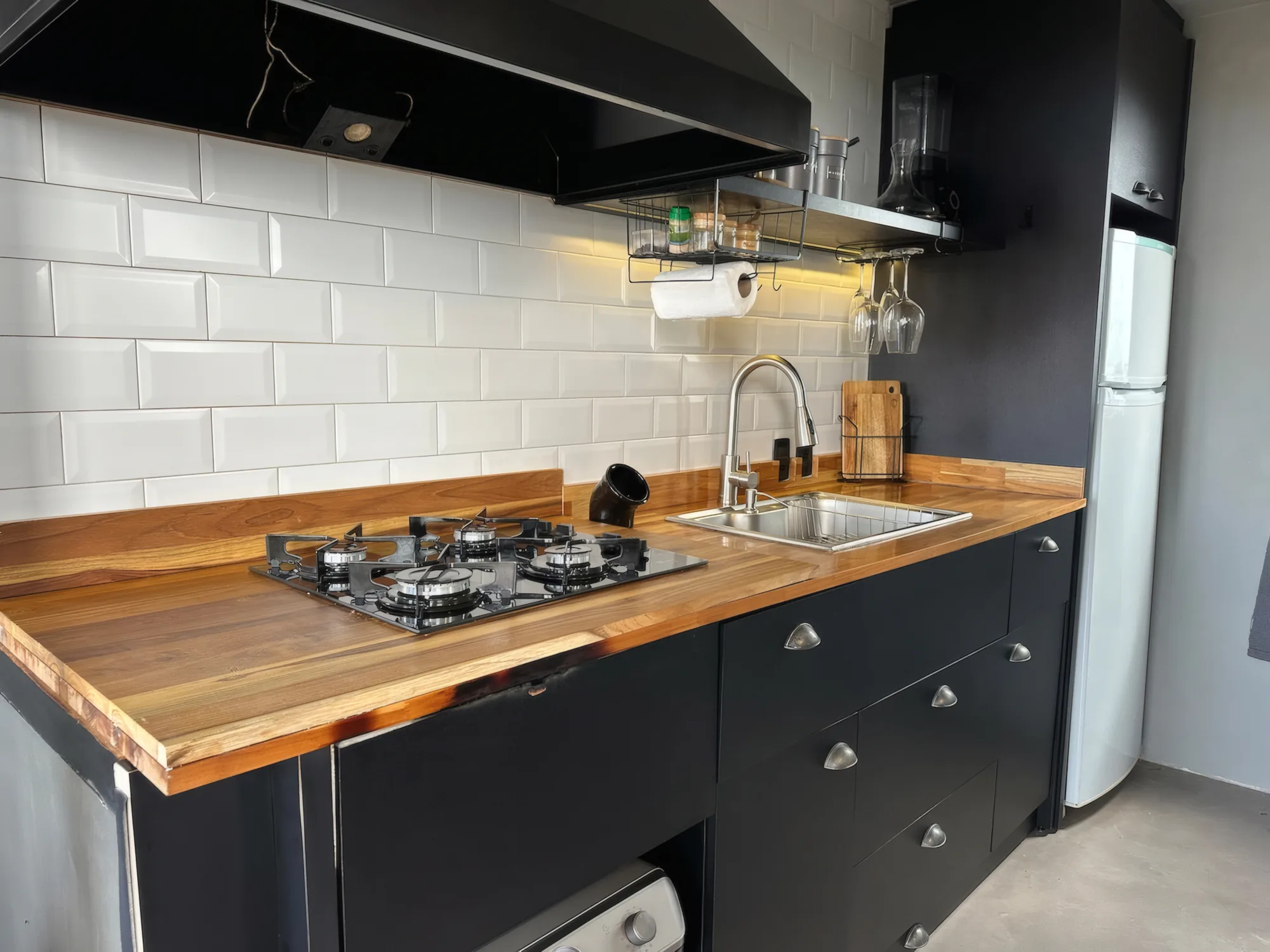 Cozinha preta com bancada de madeira, fogão e geladeira