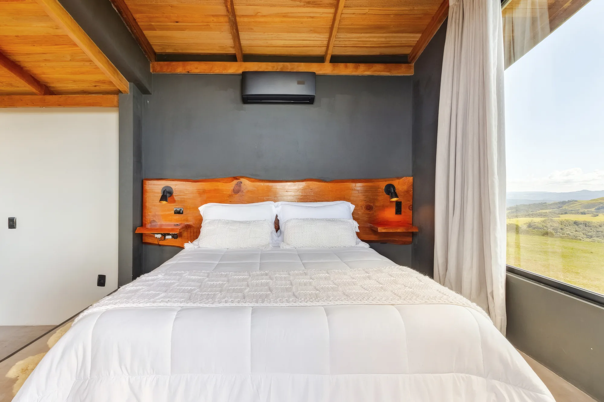 Quarto com cama queen de enxoval branco e janela para o vale