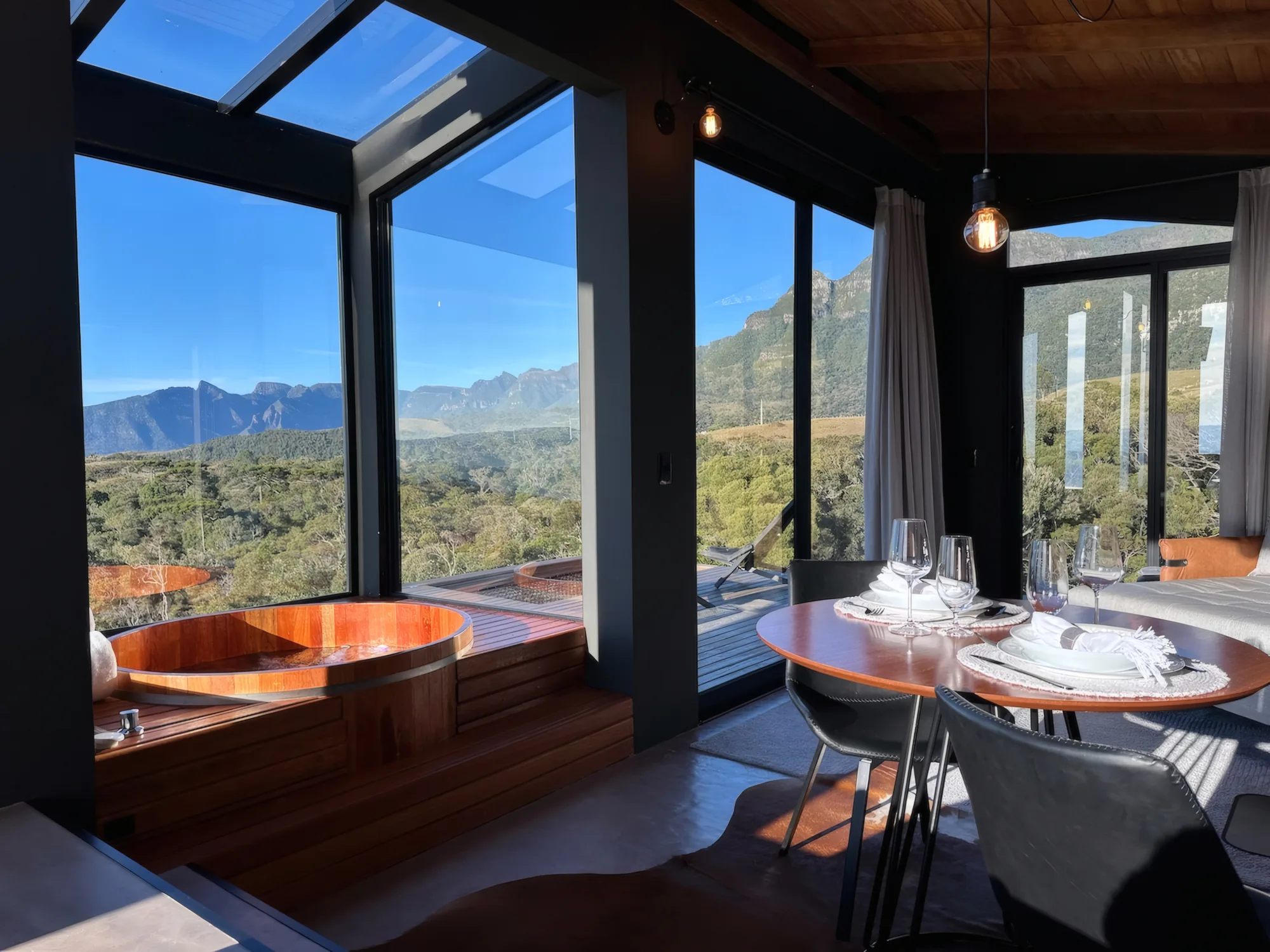 Sala envidraçada com ofurô, mesa posta e vista da serra